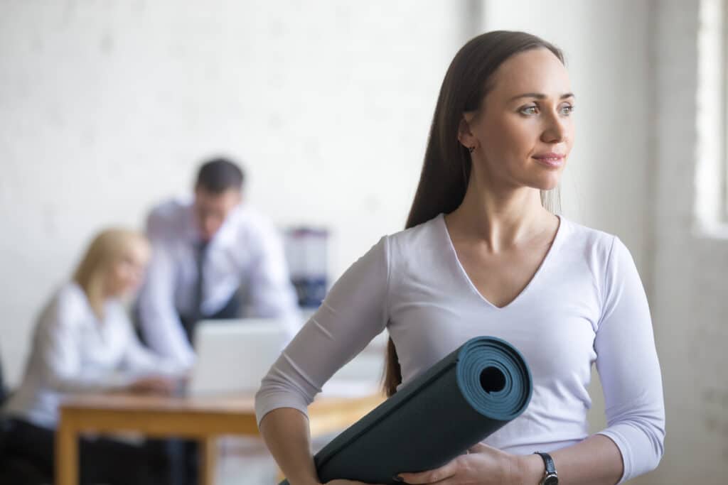 Chica que esta en una oficina cogiendo su esterilla de yoga y de camino a clase